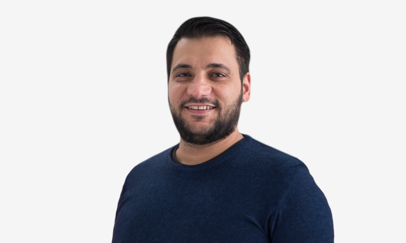 Foto van Cem Kaya in een blauwe trui voor een witte achtergrond