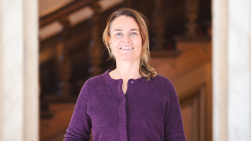 Foto Reina in een paarse trui voor een oudr, sierlijke hal met een houten trap op de achtergrond.