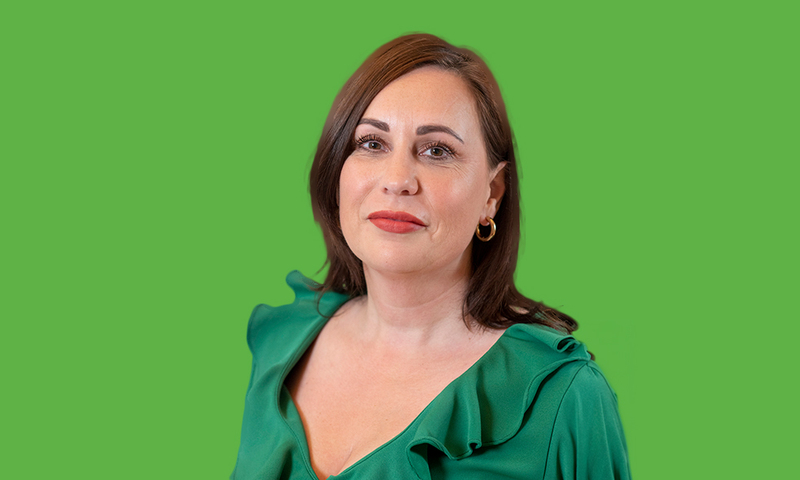 Een foto van Wieke Goudzwaard, in een groene blazer / jasje voor een groene achtergrond