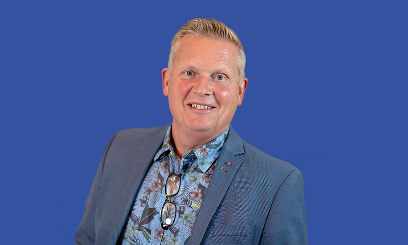 Foto van Martin van der Meulen met een grijsblauwe colbert, gekleurde blauwe overhemd. Voor een blauwe achtergrond.
