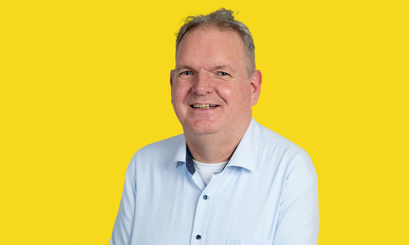 Foto van Otto van der Galiën met een lichtblauw overhemd voor een gele achtergrond.