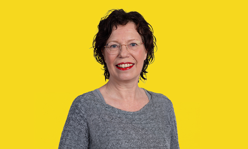 Een foto van Carina Runhart in een grijze trui voor een gele achtergrond