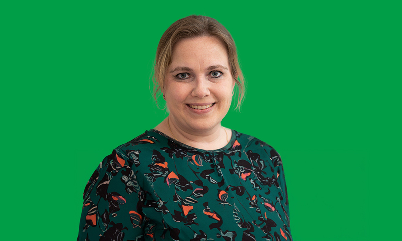 Een foto van Julie Bruijnincx in een groen met oranje patronen overhemd. Voor een groene achtergrond