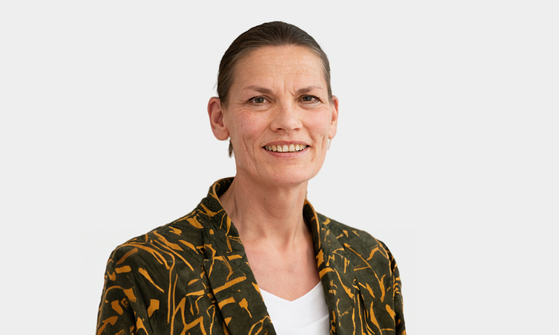 Foto van Petra Vlutters in een donkergroen en oranje colbert. Voor een witte achtergrond