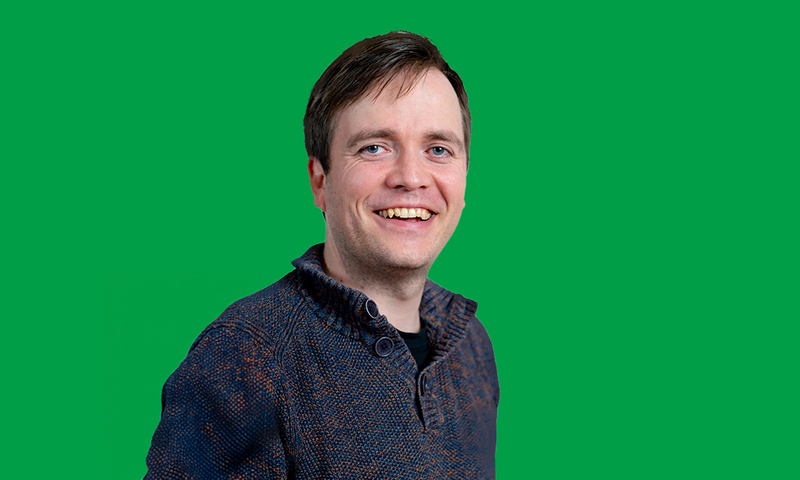 Foto van Johan Magré in een blauwe trui voor een groene achtergrond