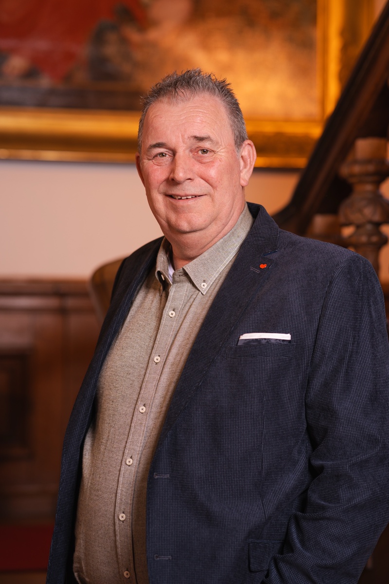 Portret foto van raadslid Jan-Willem voor een houten trap met een schilderij op de achtergrond. Een statig portret.